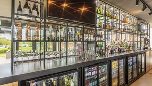 Zona de bar con estantes llenos de botellas de licor, vasos y una vitrina refrigerada.