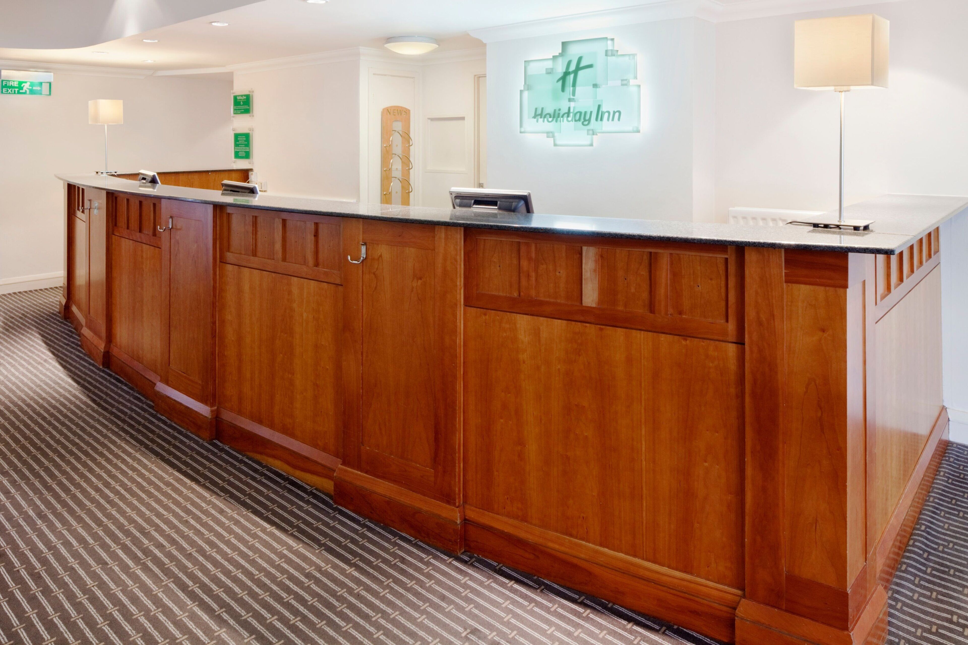 A reception desk with a wooden finish, a digital display, and a sign for Holiday Inn.