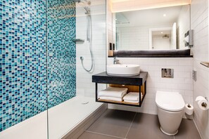 Un baño moderno con pared de mosaicos, una bañera independiente, un lavabo con encimera negra y un inodoro.