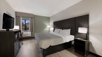 A hotel room with a bed, bedside tables, a TV, and a window with curtains.