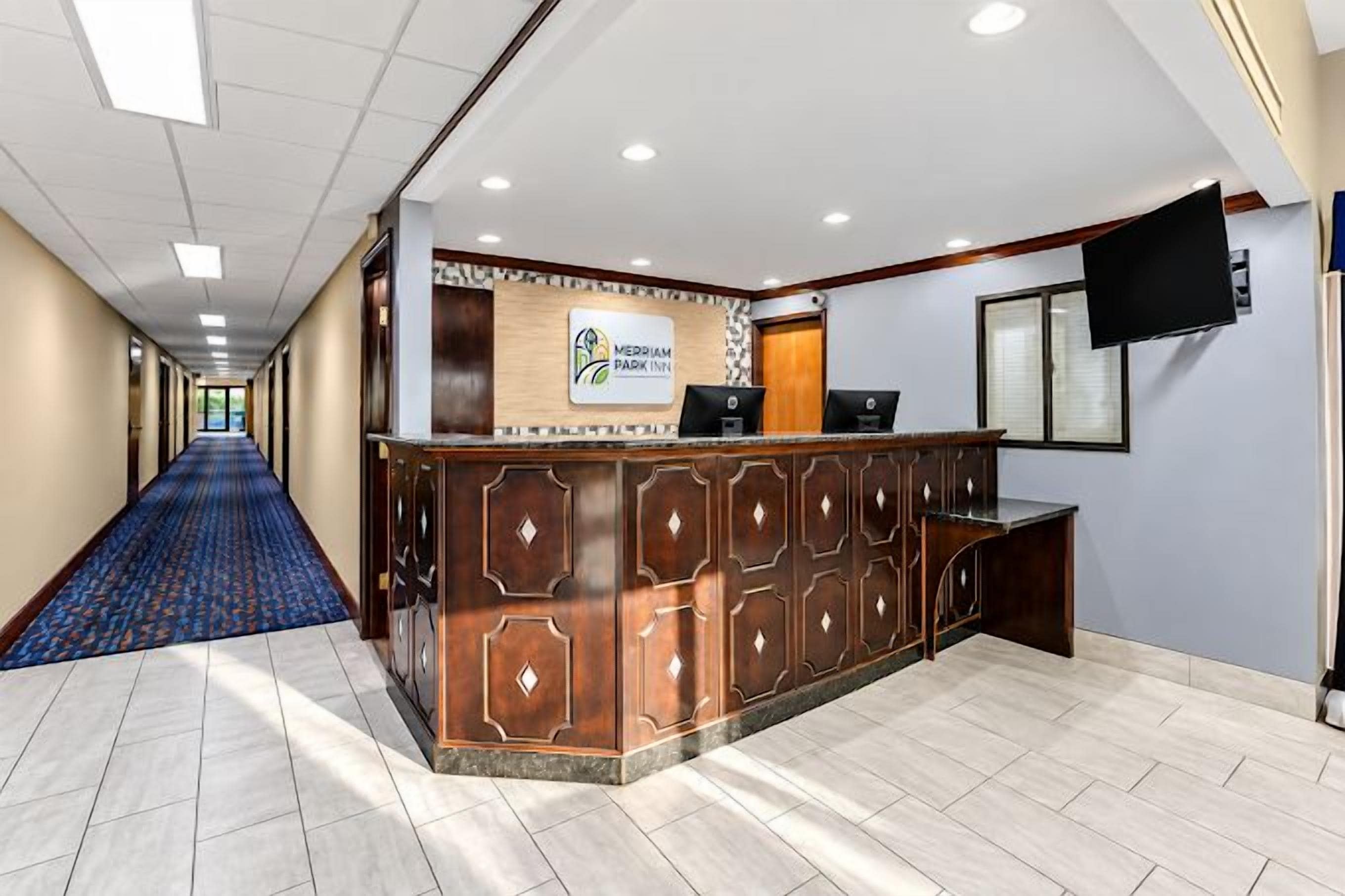 Zona de recepción de un hotel con mostrador de recepción, televisión de pantalla plana y pasillo con alfombra.