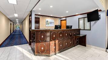 Zona de recepción de un hotel con mostrador de recepción, televisión de pantalla plana y pasillo con alfombra.