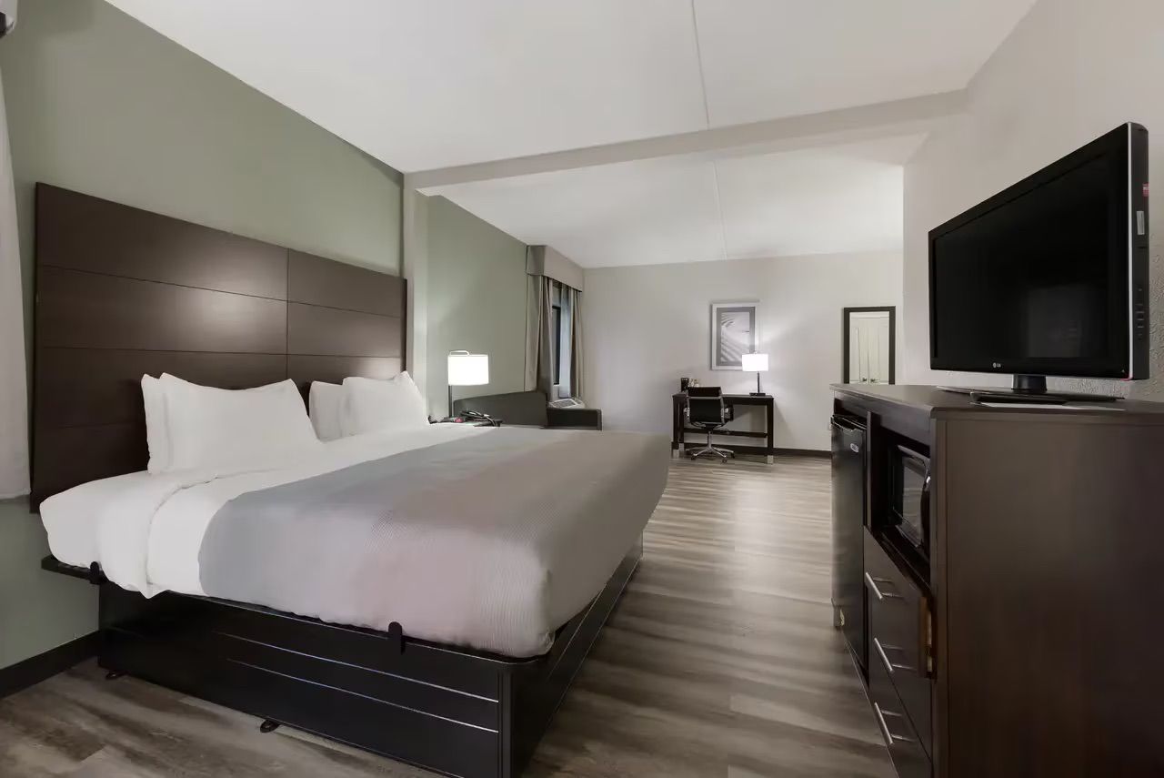 Et hotelværelse med en stor seng, et fladskærms-tv, et skrivebord med lampe og en minibar.