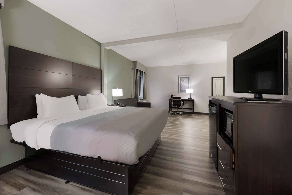 A hotel room with a large bed, a desk with a chair, a flat-screen TV, and a minibar.