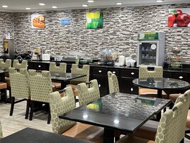 Un restaurante con diseño moderno, que presenta una pared con patrón de ladrillo, varias zonas de estar con sillas estampadas y un área de autoservicio para bebidas.