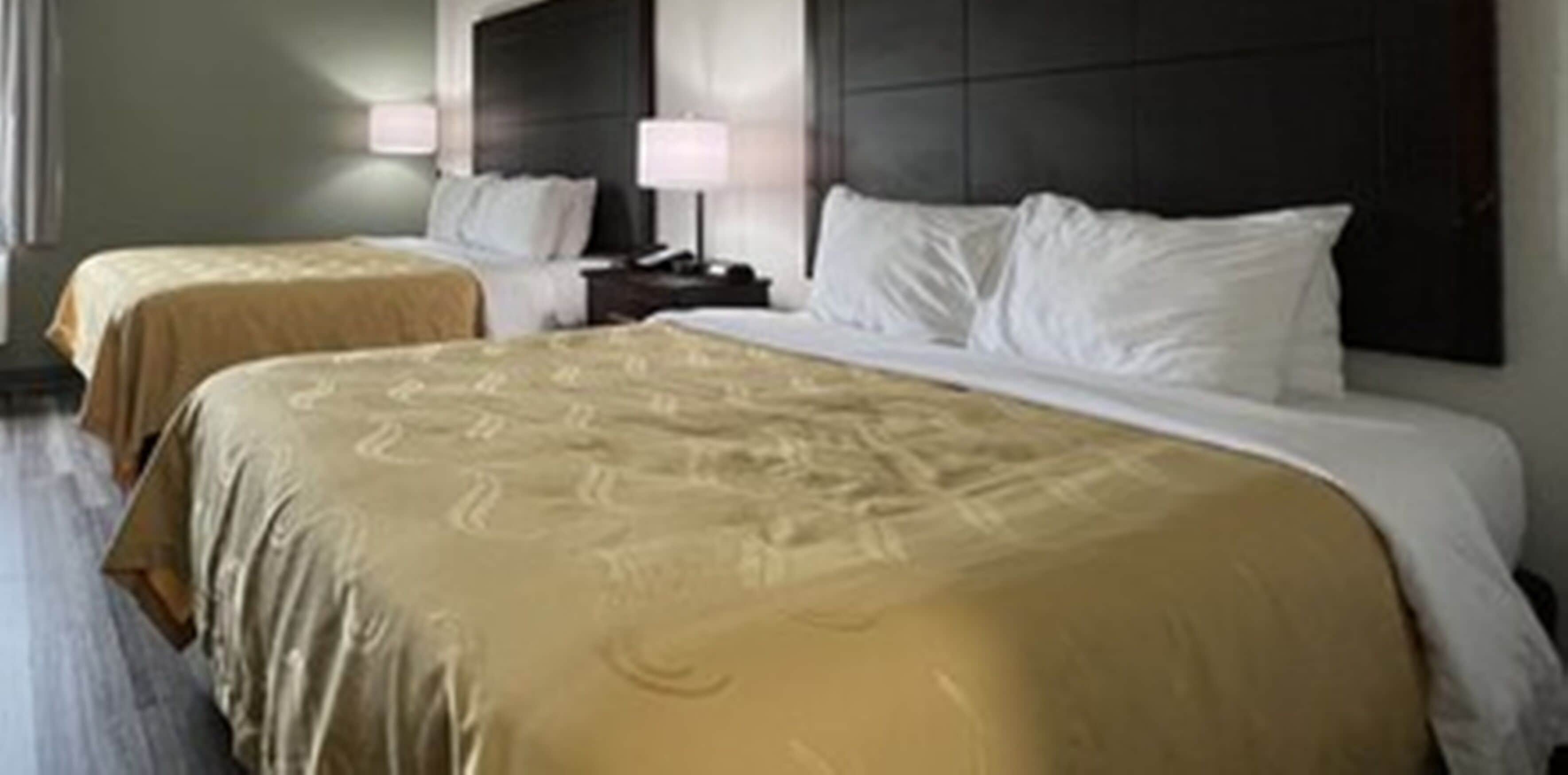 A hotel room with two beds, each with a headboard and bedside tables.