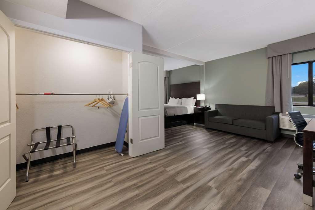A hotel room with a bed, a sofa, a desk, a chair, a wardrobe, and a door leading to another room.