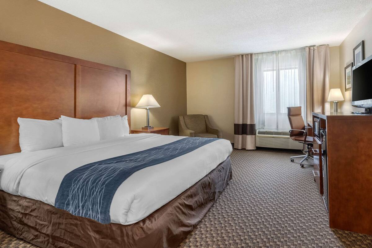 A hotel room with a large bed, a desk with a chair, a television, and a window with curtains.