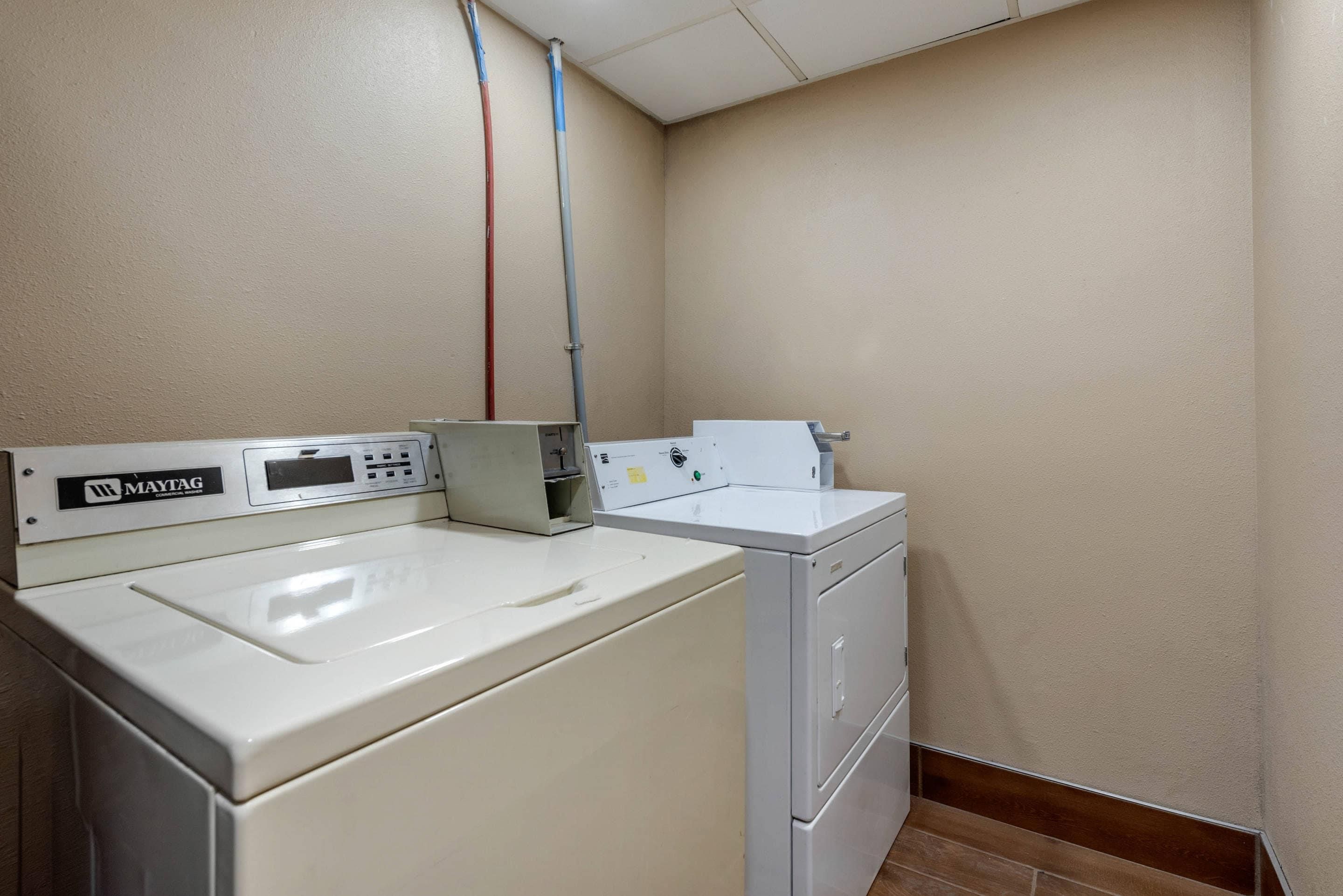 A laundry room with a Maytag commercial washer and dryer, a control panel, and a water pipe.