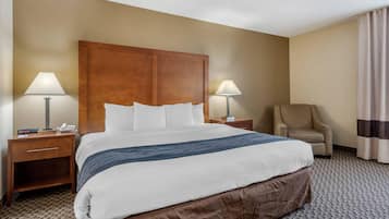 A hotel room with a large bed, two bedside tables with lamps, a chair, and a curtain.