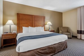 Ein Hotelzimmer mit einem großen Bett, zwei Nachttischen mit Lampen, einem Sessel und einem Vorhang.