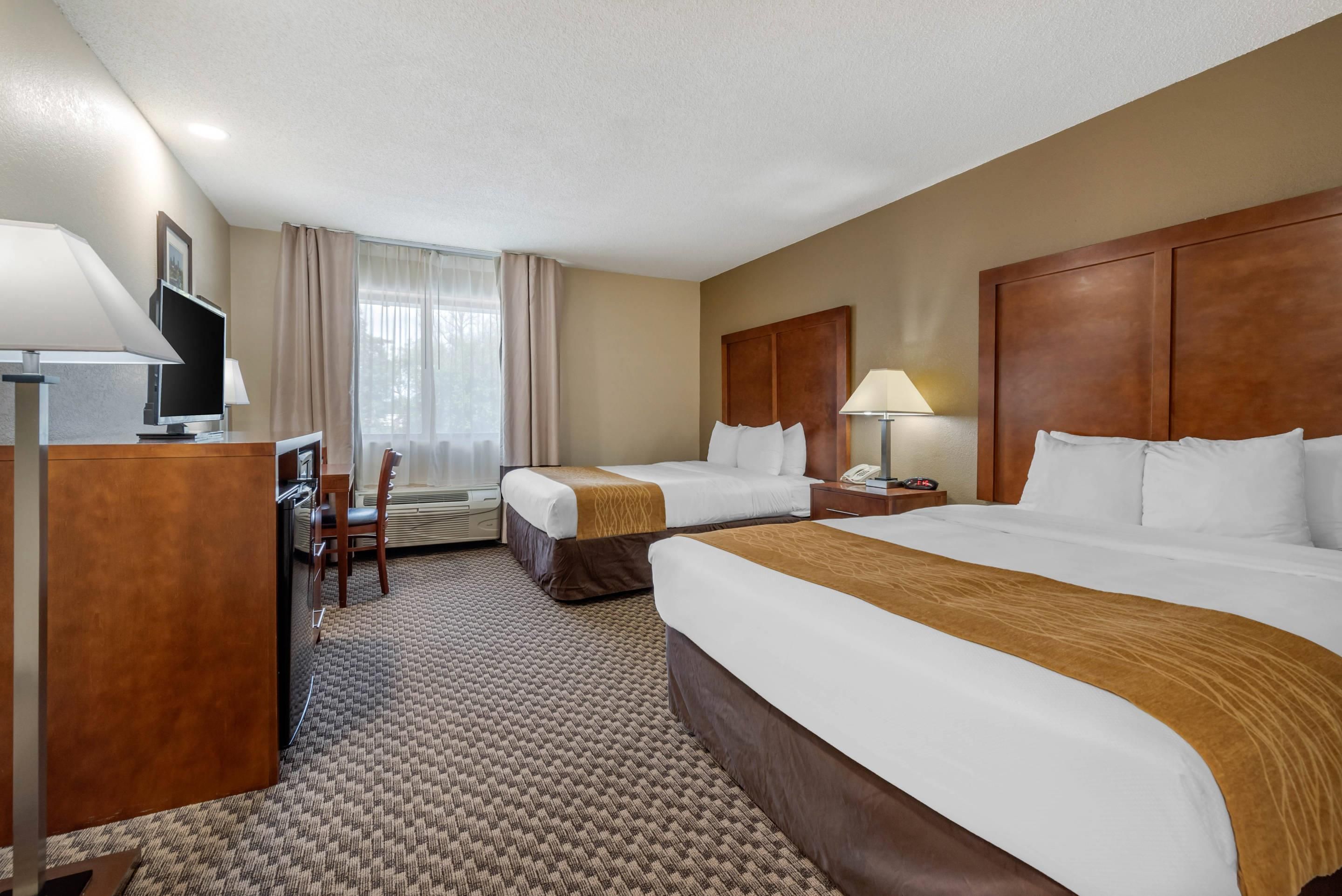 A hotel room with two beds, a desk, a chair, a TV, and a window with curtains.