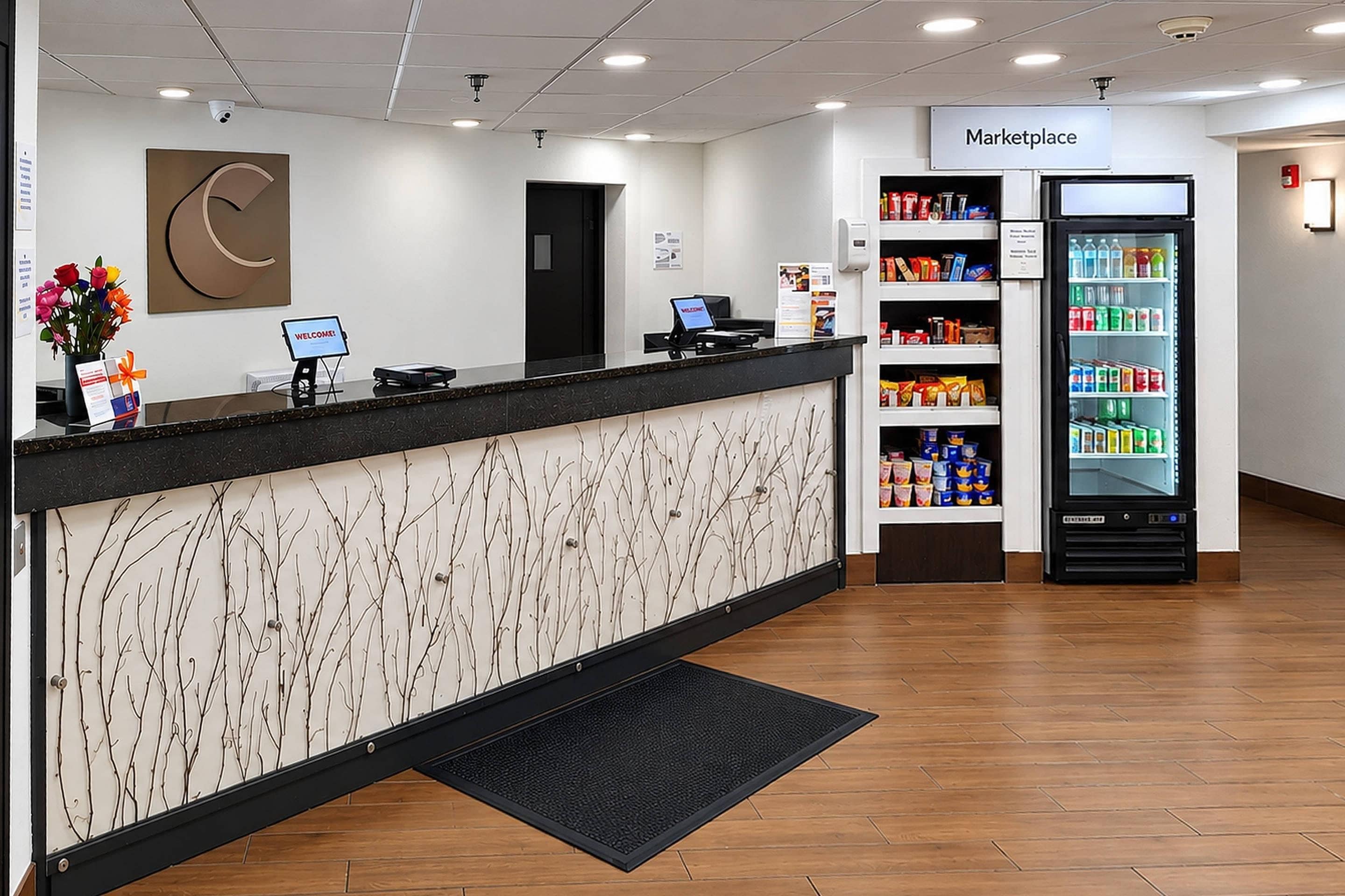 A reception area with a counter, a computer, a sign reading 'Welcome!', and a refrigerator stocked with beverages.