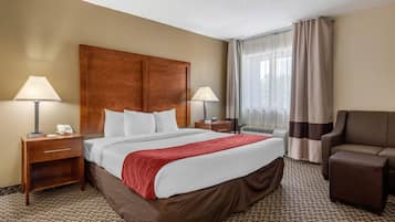Une chambre d’hôtel avec un grand lit, deux tables de chevet avec des lampes, une chaise et une fenêtre avec des rideaux.