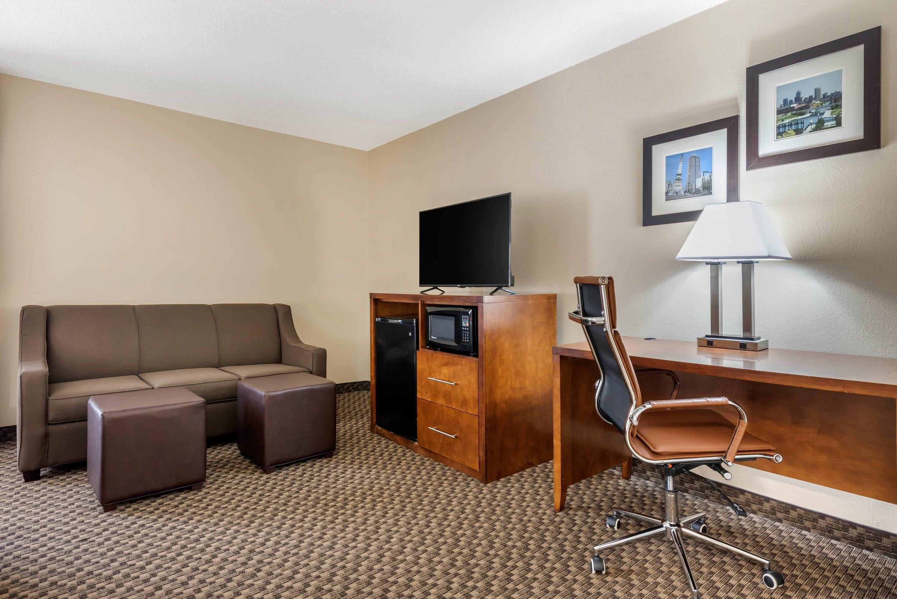 A hotel room with a sofa, a desk with a chair, a flat-screen TV, a microwave, and a lamp.