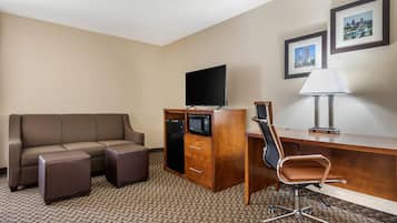 A hotel room with a sofa, a desk with a chair, a flat-screen TV, a microwave, and a lamp.