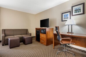 Une chambre d’hôtel équipée d’un canapé, d’un bureau avec une chaise, d’un téléviseur à écran plat, d’un four à micro-ondes et d’une lampe.