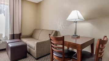 Una habitación de hotel con sofá, una mesita con lámpara, una silla y un reposapiés.