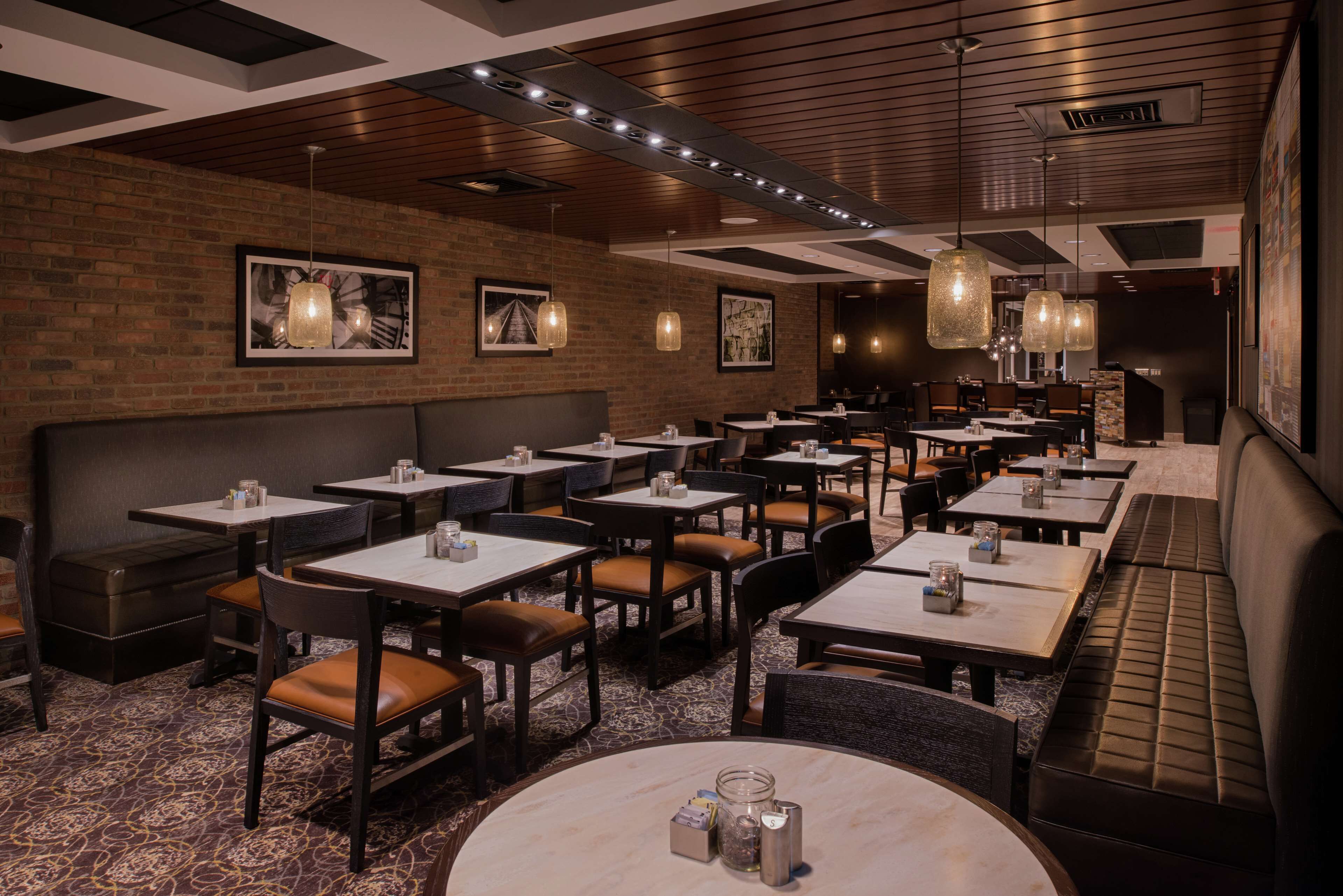 A restaurant with multiple tables and booths, brick walls, and hanging pendant lights.