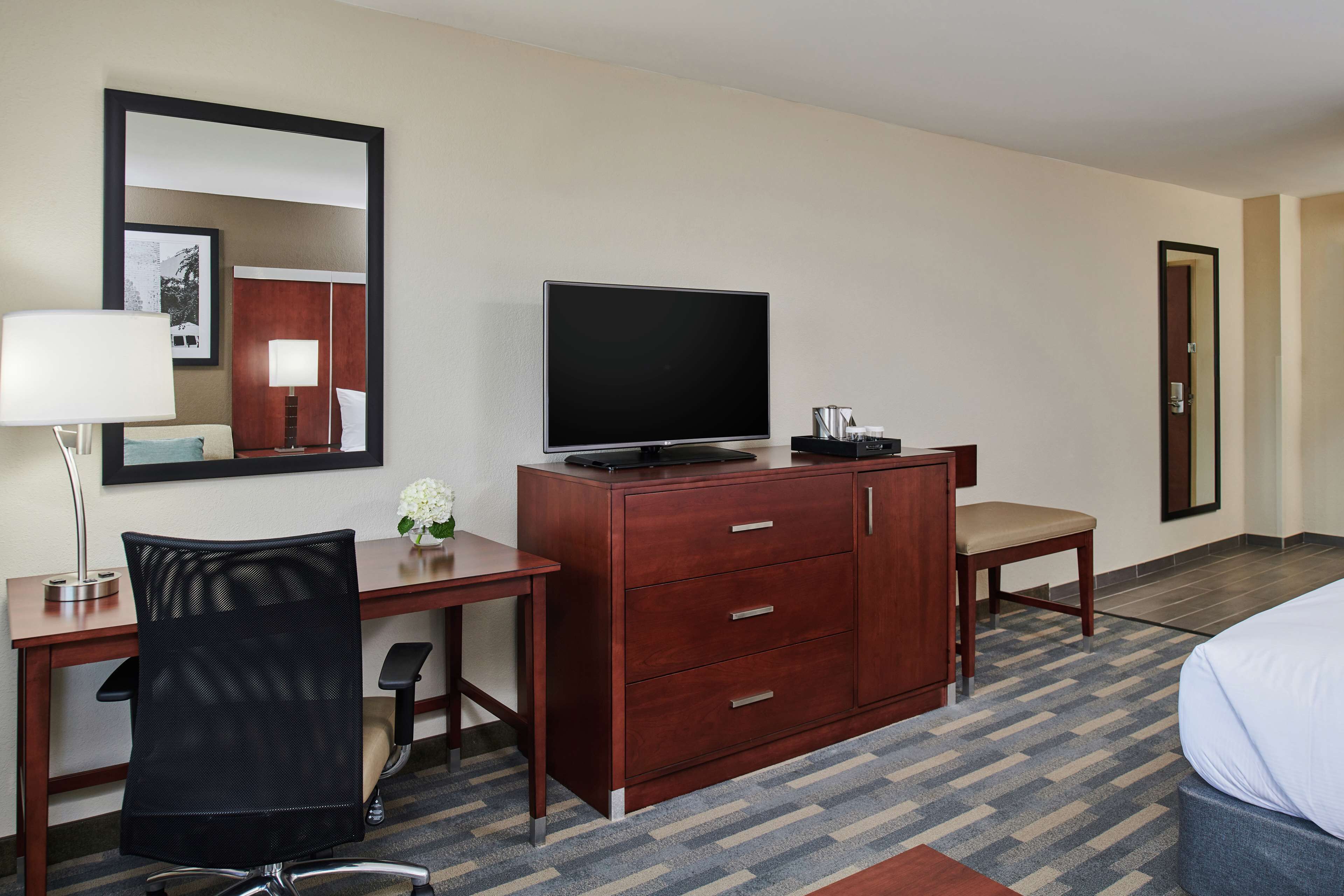 A hotel room with a wooden desk, a television, a chair, a bed, and a mirror.
