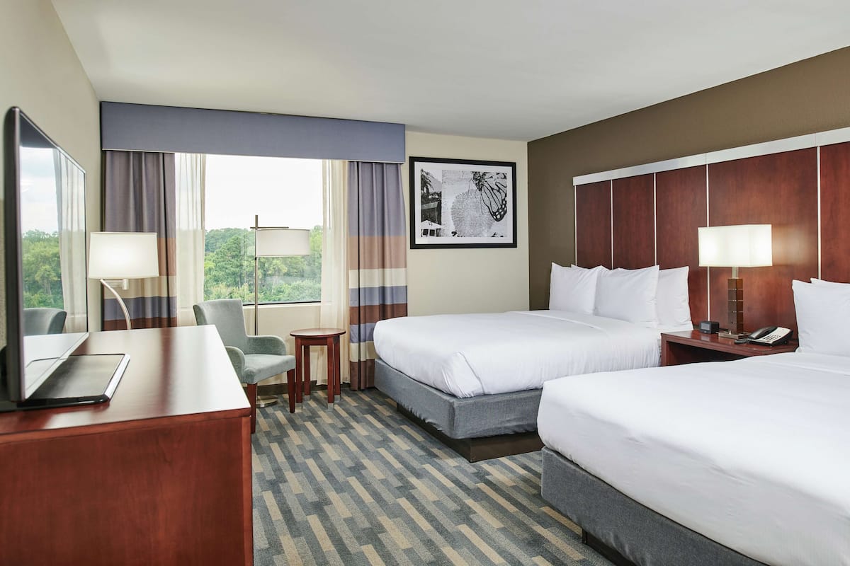 Une chambre d’hôtel avec deux lits, un bureau avec un ordinateur portable, une chaise, une petite table et une fenêtre avec des rideaux.