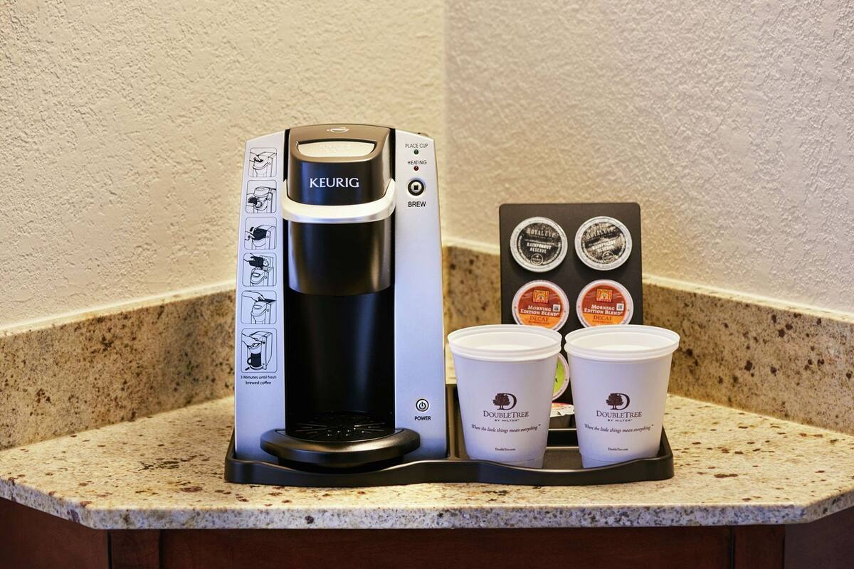 Une machine à café Keurig avec un compartiment pour les dosettes de café et deux gobelets jetables, posée sur un comptoir de cuisine.