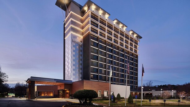 A modern hotel with a prominent corner entrance, large windows, and a well-lit facade. - DoubleTree by Hilton Raleigh Crabtree Valley (Raleigh)
