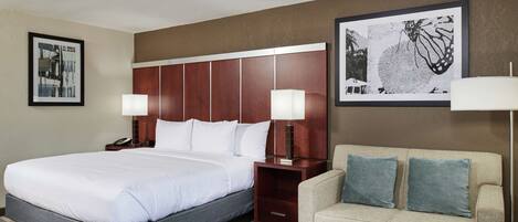 A hotel room with a large bed, a sofa, a nightstand with a lamp, and two framed pictures on the wall.
