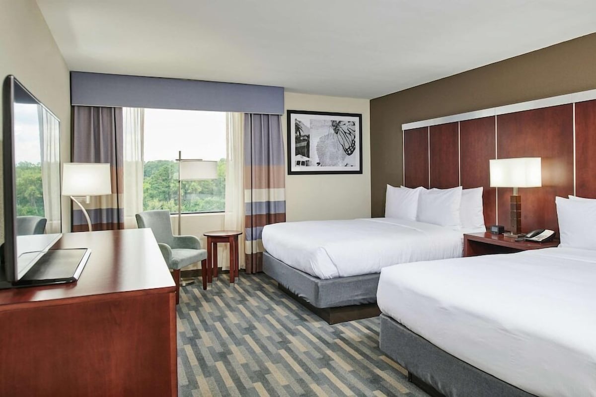A hotel room with two beds, a desk, a chair, a small table, and a window with curtains.