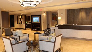 A lobby with seating, a reception desk, a television, and a clock on the wall. - DoubleTree by Hilton Raleigh Crabtree Valley (Raleigh)