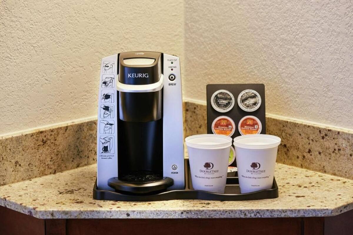A Keurig coffee maker with a coffee pod holder and two disposable cups on a countertop.