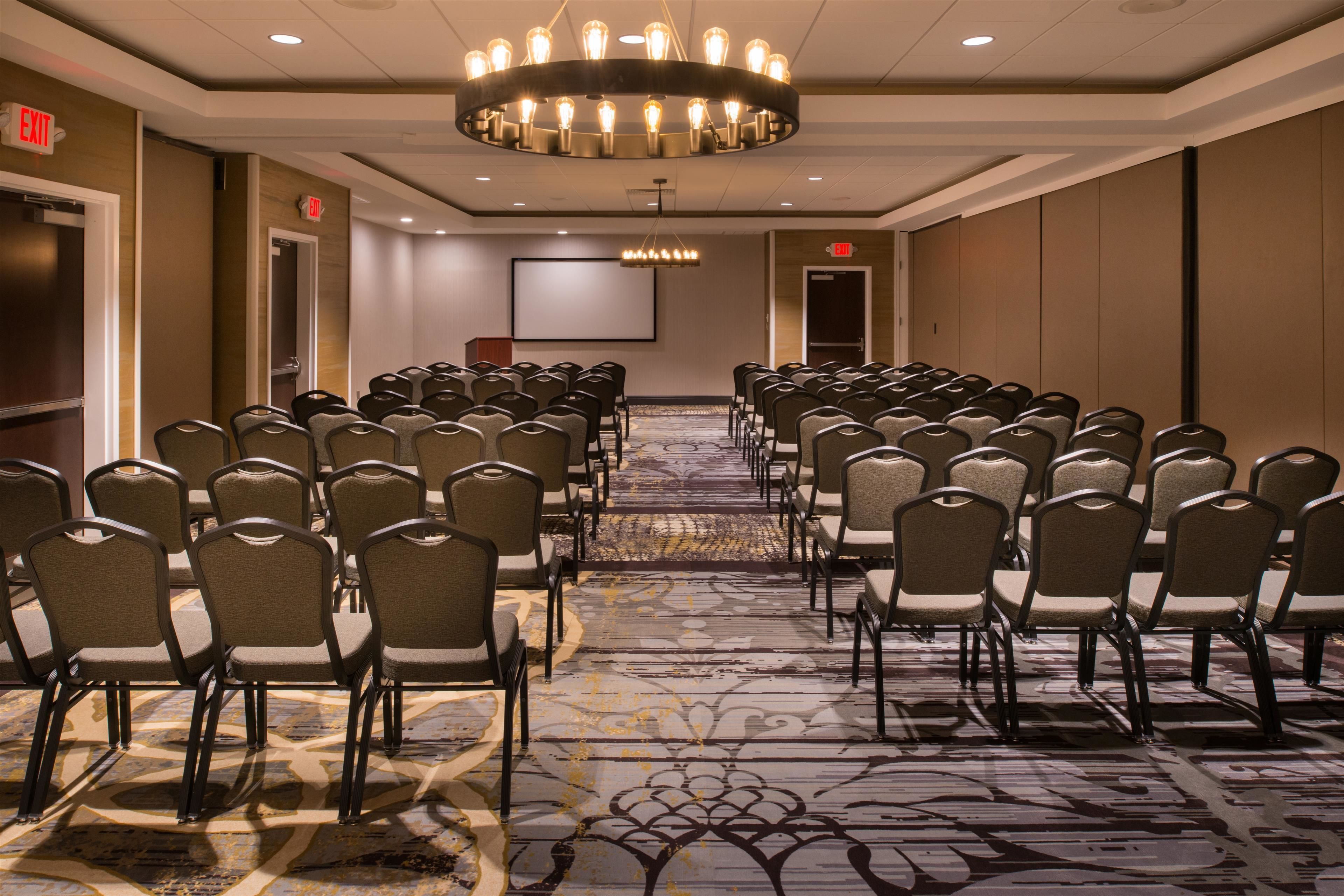 A conference room with rows of chairs, a projector screen, and a large chandelier.