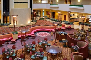 Un vestíbulo de hotel con una zona de estar central, varias mesas de comedor y un diseño decorativo en el suelo.