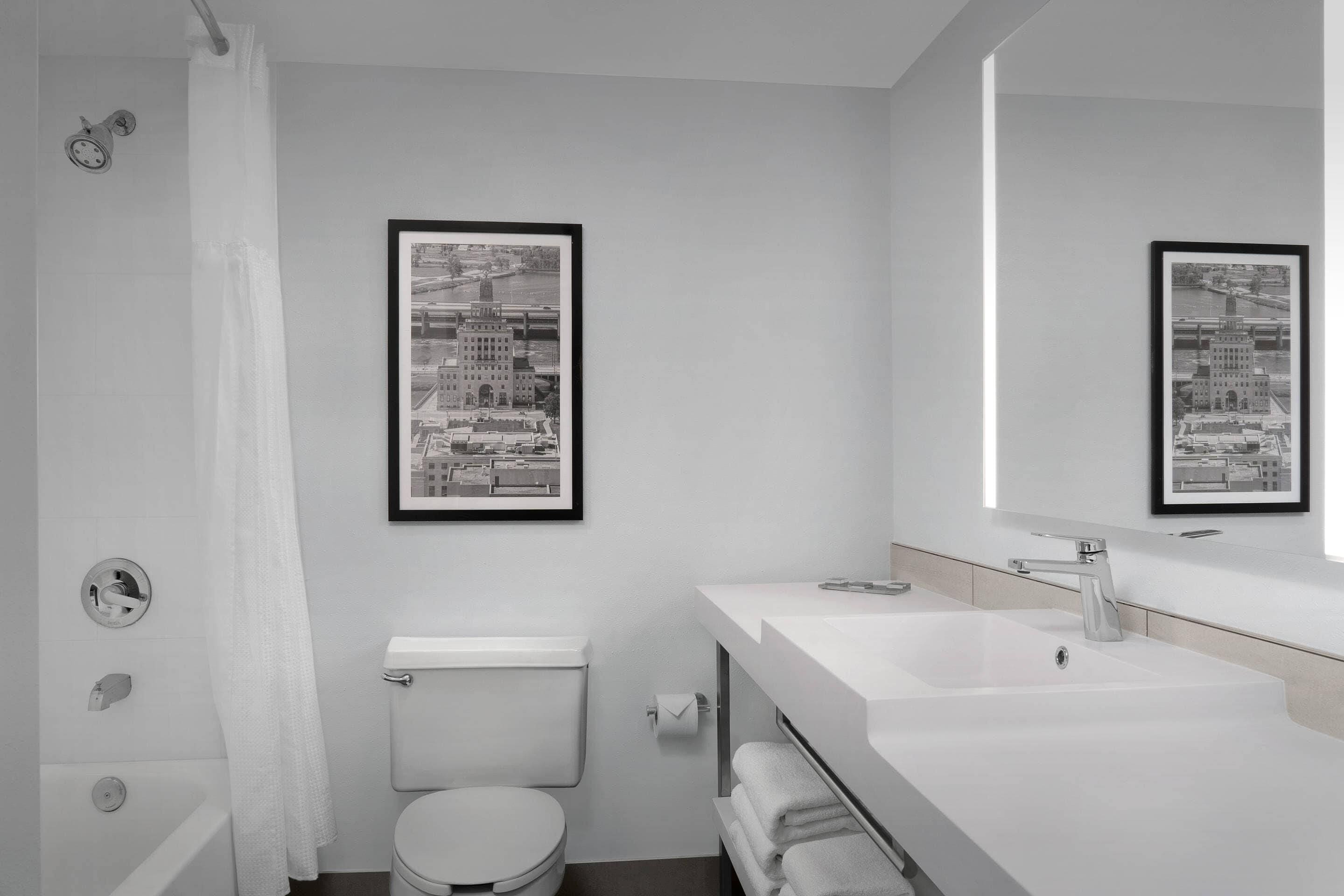 Une salle de bain moderne équipée de toilettes, d’un lavabo et d’une douche. Deux photographies en noir et blanc, encadrées, sont accrochées au mur.