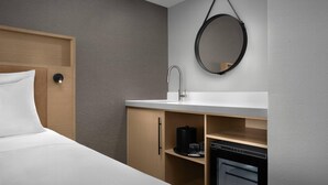 A hotel room with a bed, a wooden wardrobe, a sink, a mirror, and a coffee machine. - Radisson Hotel Cedar Rapids (Cedar Rapids)
