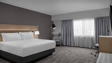 Ein Hotelzimmer mit einem großen Bett, einem Schreibtisch, einem Stuhl und einem Fenster mit Vorhängen.