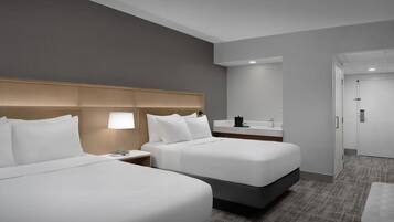 Habitación de hotel con dos camas, una mesita de noche con lámpara, un escritorio pequeño con espejo y una puerta.
