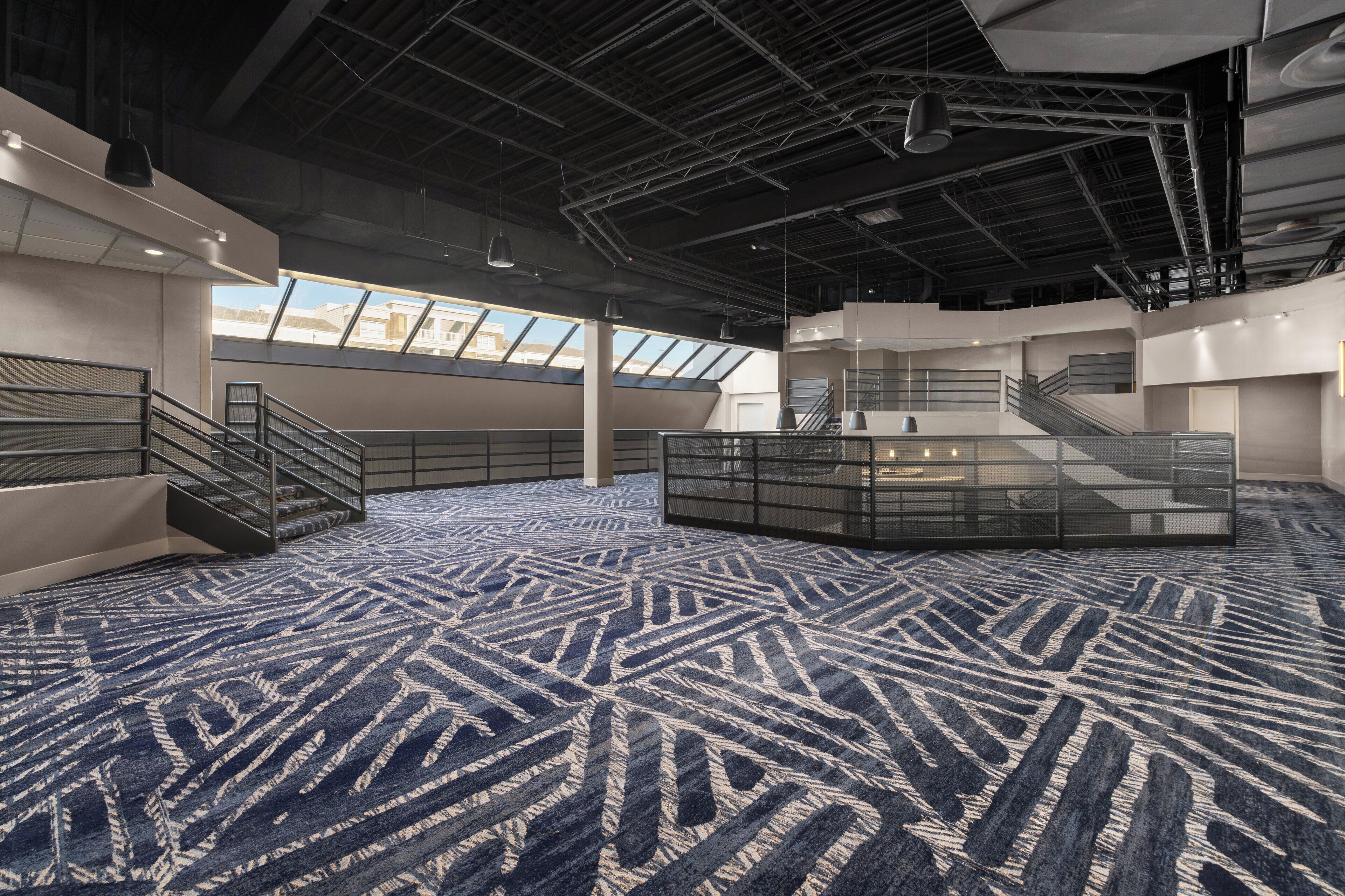 A spacious indoor area with a patterned carpet, multiple staircases, and a glass partition.