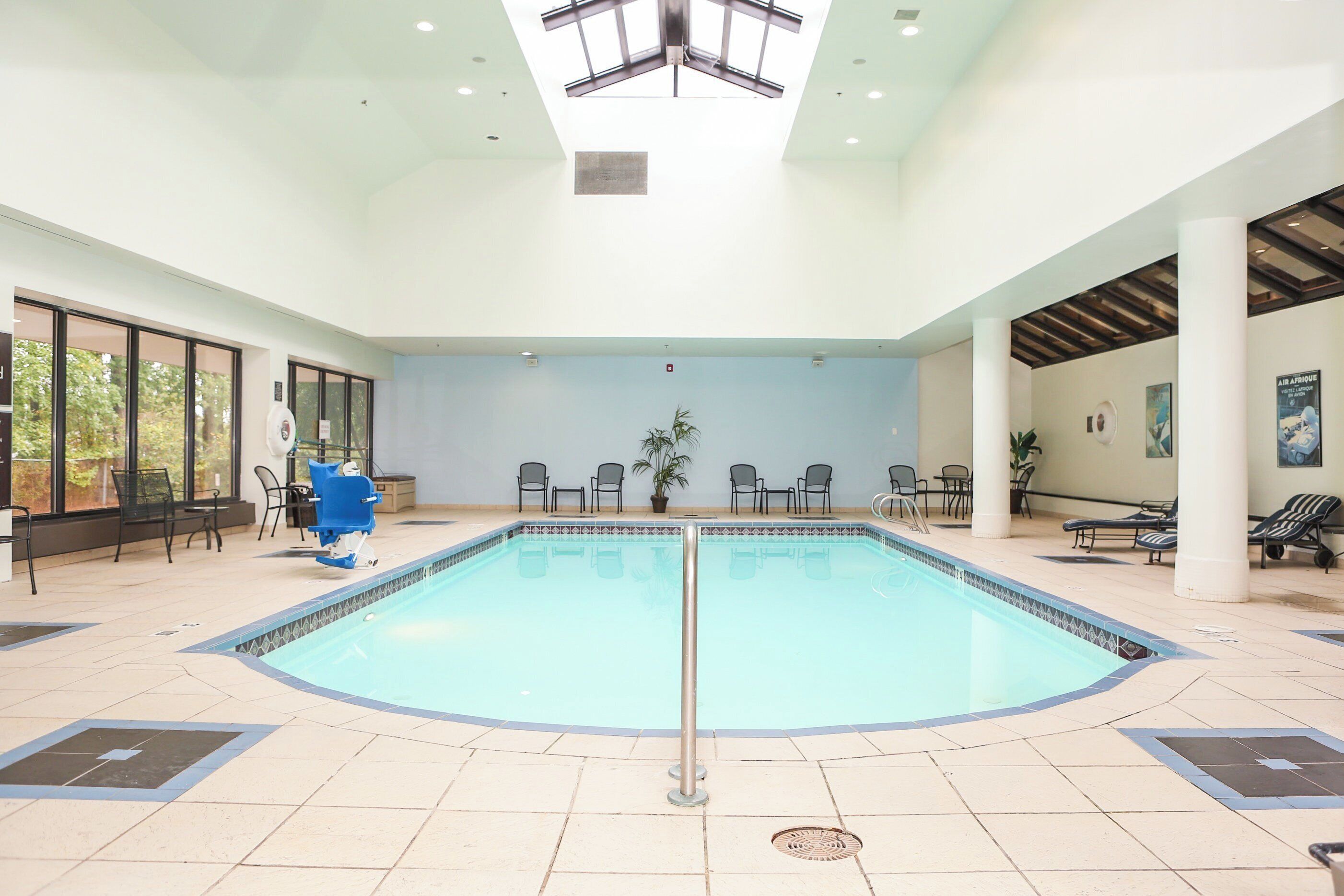 An indoor swimming pool with a tiled floor, surrounded by lounge chairs and tables.