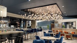 Uma área de bar moderna com diversas opções de assento, incluindo banquetas e mesas redondas, e um alto teto com um lustre único.