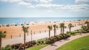 Uma praia com calçadão pavimentado, palmeiras e guarda-sóis.