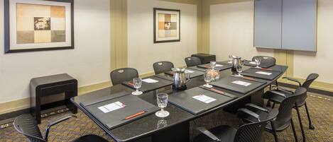 A conference room with a long table, chairs, a projector screen, and framed artwork on the walls.