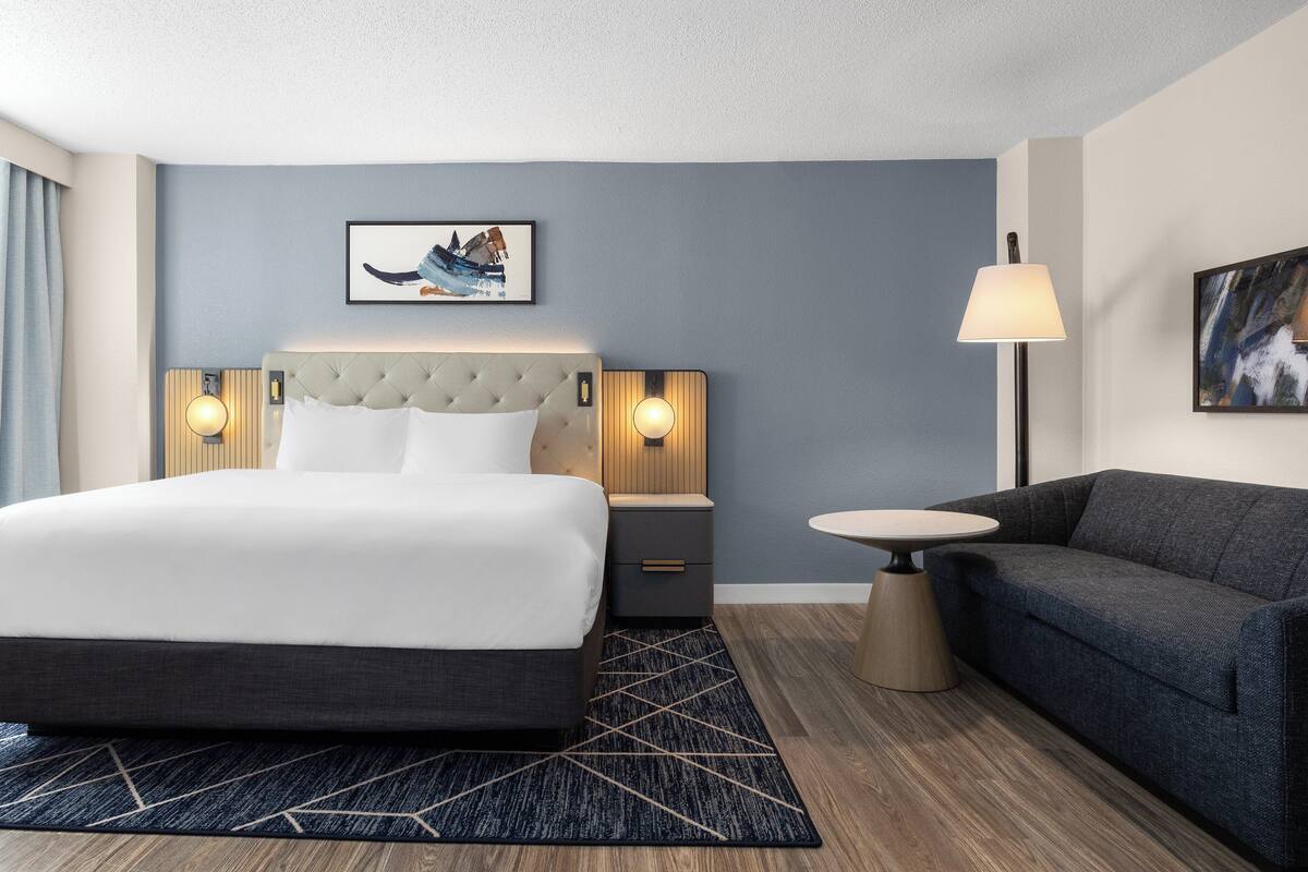 Ett hotellrum med en stor säng, en soffa, ett litet bord och två väggmonterade lampor.