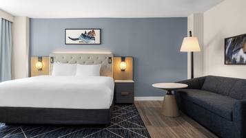Una habitación de hotel con una cama grande, un sofá, una mesita y dos lámparas de pared.