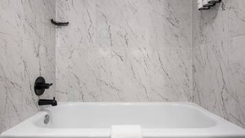 Un baño moderno con pared de mármol, una bañera y un perchero para toallas.