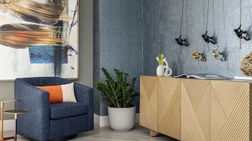 Una sala de estar moderna con un sillón azul, una planta en maceta, un mueble de madera y una pared con arte abstracto y adornos colgantes.