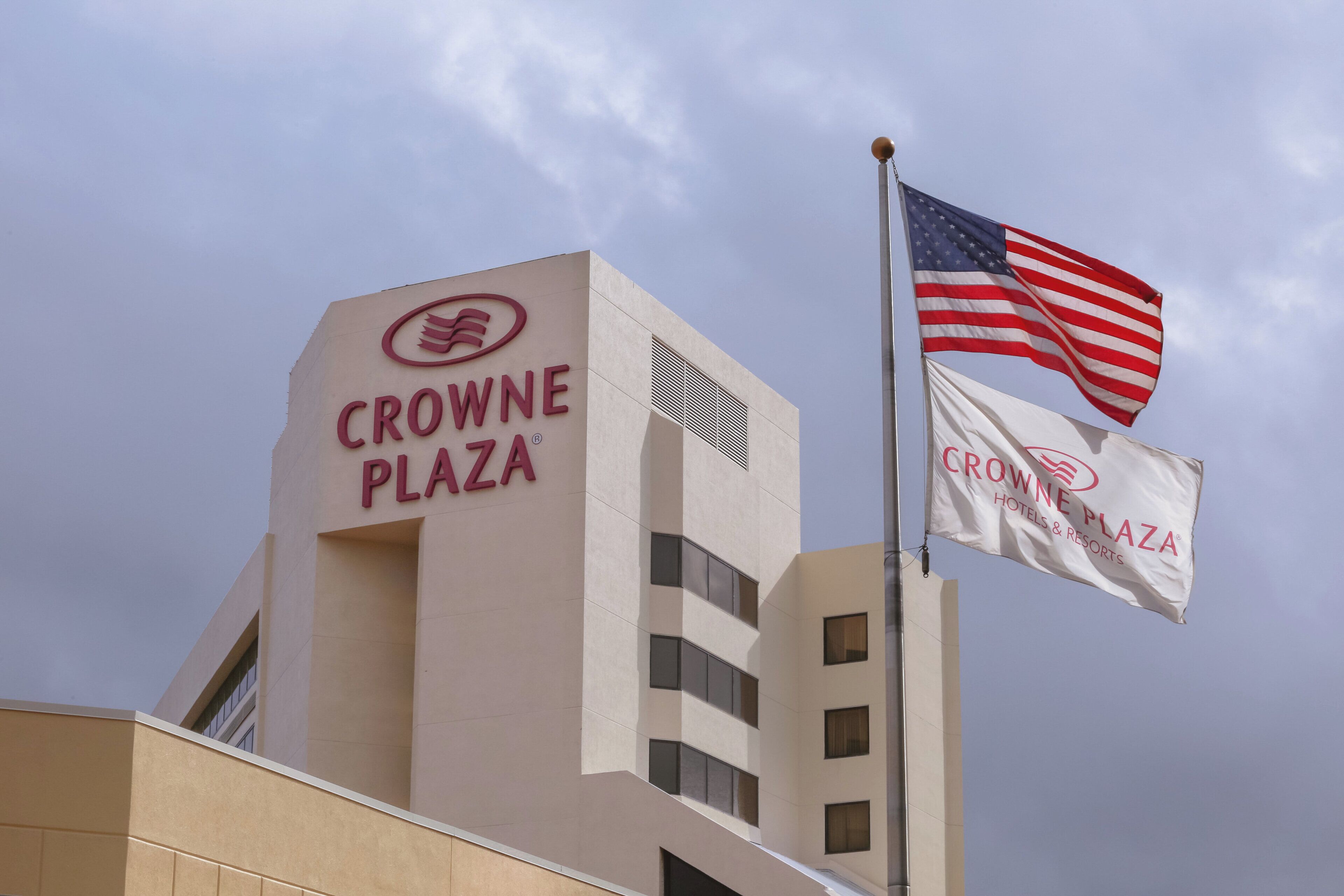 A building with a sign reading 'CROWNE PLAZA' and two flags, one of which is the American flag.