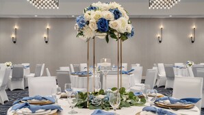Mesa de banquete posta para um evento formal, com toalhas brancas, pratos de sousa dourados e guardanapos azuis.