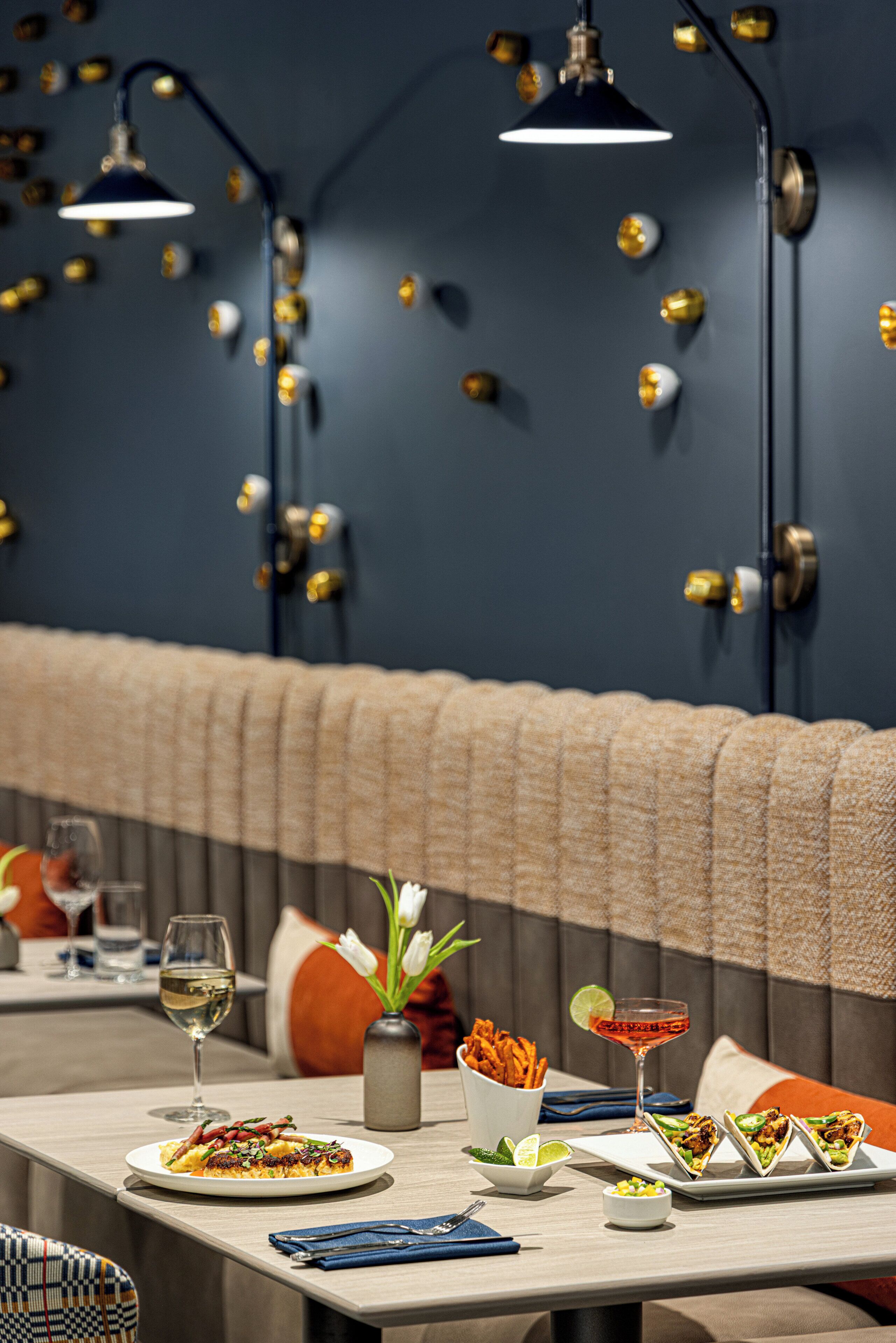 A restaurant setting with a table set for dining, including plates of food, a glass of wine, and a cocktail.