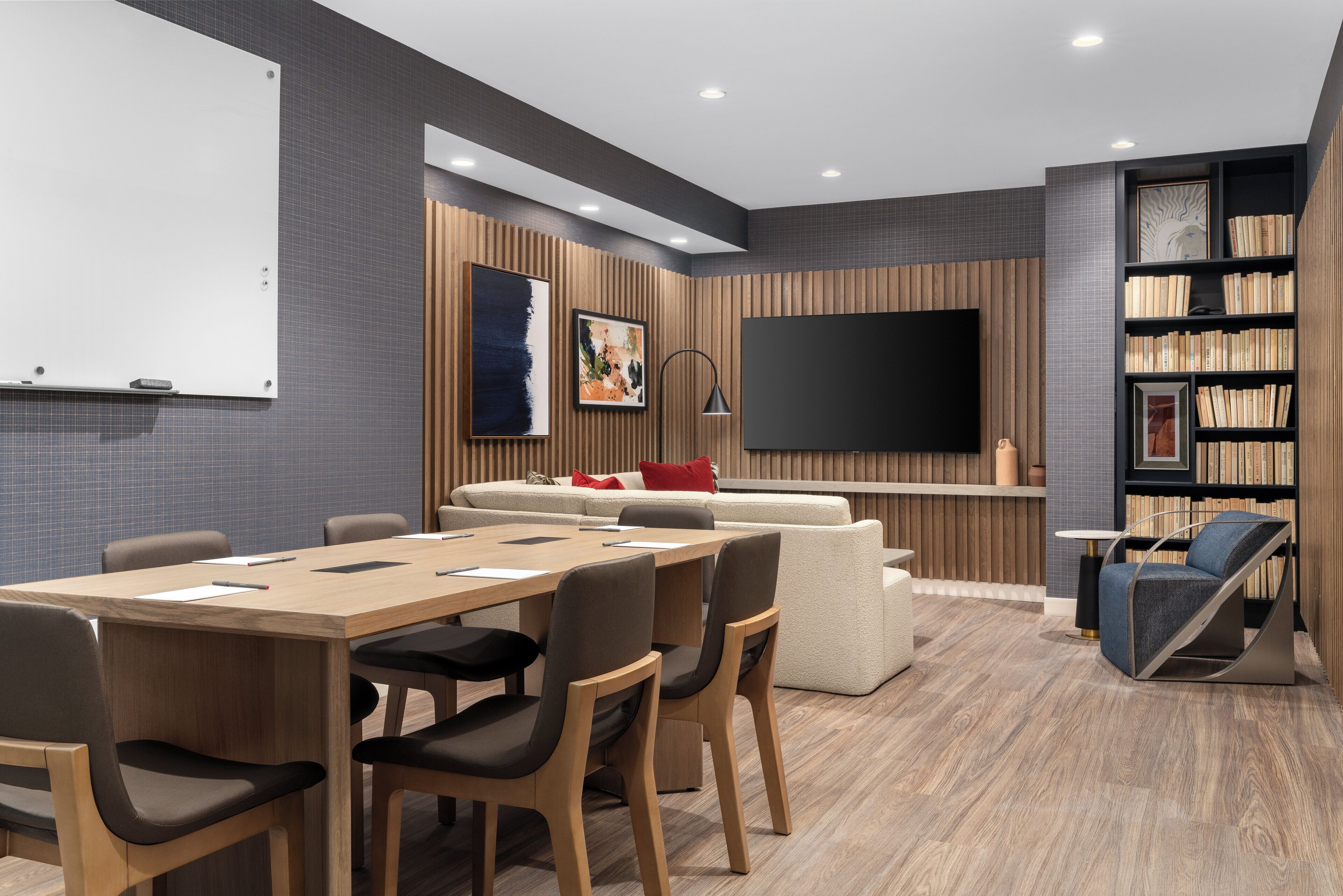 Una sala de reuniones moderna con una mesa de madera, sillas, una pizarra, un televisor de pantalla plana grande, un sofá y una estantería.